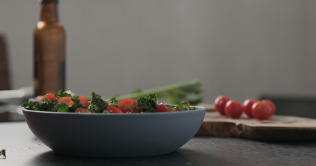 Slow motion man hands put tomatoes on top of kale in blue bowl on concrete surface