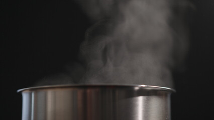Steam rising from pot over black background