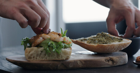 man making ciabatta sandwich with shrimps, olives and pesto