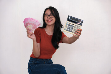 Cheerful Asian woman sitting and showing some cash money and a calculator in both hands