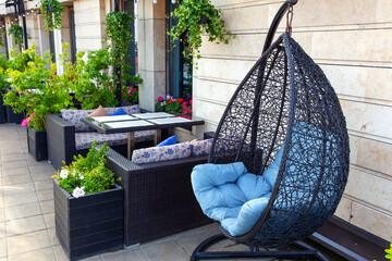 Hanging cocoon chair among living plants on the terrace of residential building - obrazy, fototapety, plakaty