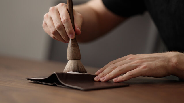 man cleaning leather wallet on wood table