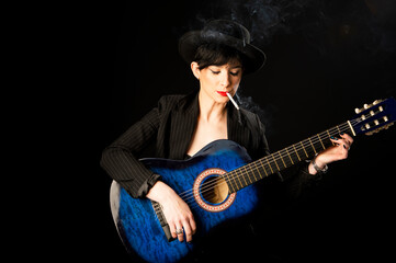 Obraz premium Young beautiful woman in black with a cigarette and an acoustic blue guitar