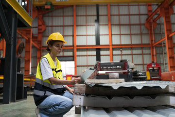 Female factory worker using digital tablet checking galvanized or metal sheet in warehouse storage....