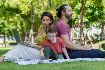 Fototapeta premium Happy family day. Father, mother use laptop and tablet. Son and Caucasian enjoy watercolor painting and picnic in nature.