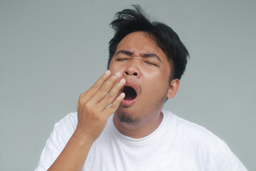 Close up of an asian man with sleepy expression and yawn with messy hair. Wake up concept. With a...
