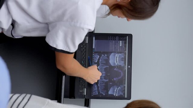 Female dentist and her patient are looking at teeth X-ray on laptop, discussing treatment options. Image shows professional dental consultation and decision-making process.