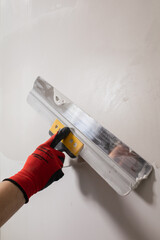 Leveling the wall surface with white putty and a spatula is the work of a qualified painter and finisher