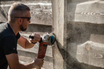 A man with a powerful tool with an angle grinder cleans the wood of the fence - grinding the boards...