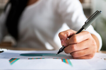 hand of woman holding pen with writing on paper report in office