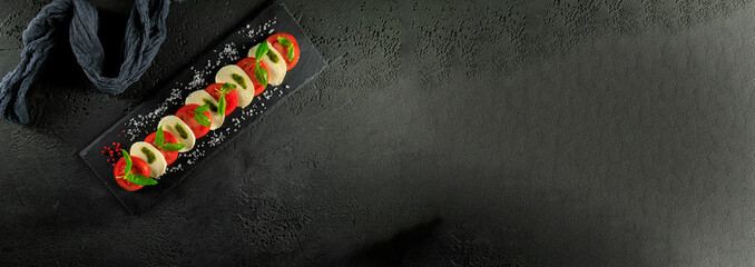 Italienischer Tomaten und Mozzarella Salat mit Basilikum, Olivenöl auf dunklen Hintergrund...