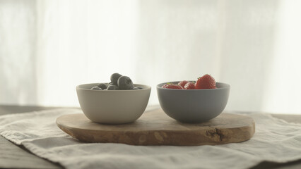 fresh blueberries and strawberries in ceramic bowls with natural light - obrazy, fototapety, plakaty