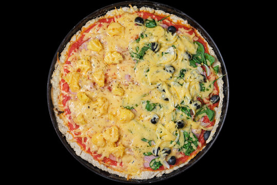 Homemade pizza with cheese, pineapple, spinache, ham, tomato, olives, onion in pizza pan. Shot from above on black background