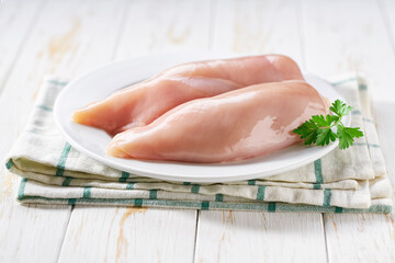 Raw chicken fillet with parsley in a plate on a wooden table. © Igor Dudchak