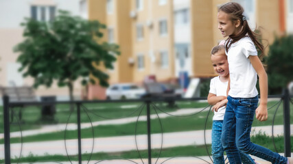 Girls play and run a race on the lawn outdoor street at the playground. Children's outdoor games. Modern residential buildings on background.