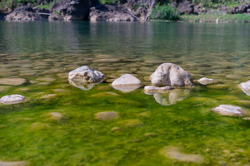 Obraz premium flowing water in a calm river where there are rocks in the water. River water surface details, reflections and abstracts, ripples and patterns.