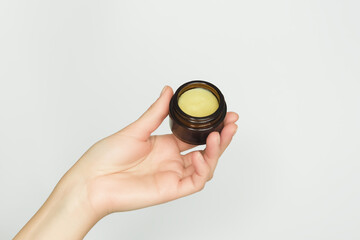 a woman's hand holds natural cosmetic solid oil in a glass jar. natural skin care concept