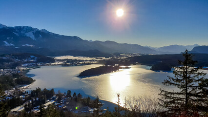 Panoramic sunset view on Lake Faak from Taborhoehe in Carinthia, Austria, Europe. Surrounded by high snow capped Austrian Alps mountains. Surface of lake is frozen. Alpine Landscape in frosty winter