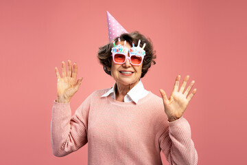 Smiling beautiful senior 70 years old woman wearing funny wearing eyeglasses hands up isolated on...