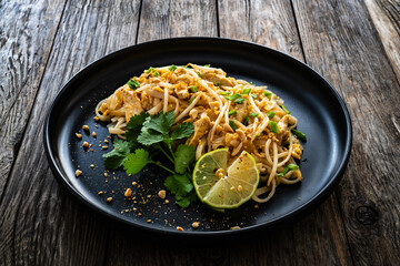 Pad Thai with chicken nuggets and rice noodles in peanut and tamarind sauce on wooden table
