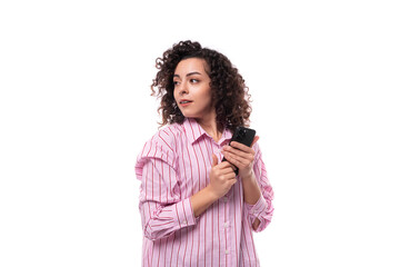 young brunette curly caucasian woman dressed in a striped pink shirt holds a telephone in her hand and looks away