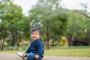 Fototapeta premium 屋外の自然あふれる公園内で楽しそうに笑顔で遊ぶファーストシューズを履いた1歳の幼児