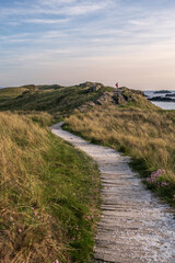 Fototapeta na wymiar A path, leading through grassy sand dunes, to a ridge overlooking the ocean. it is evening and the scene is bathed in golden light. Angelsey, Wales