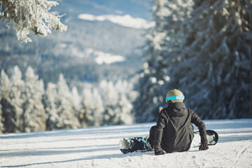 Snowboard sportsmen sitting on snow. One snowboarder ready for snowboarding on winter mountain top. Back of snowboarder with snowboard on winter mountain top
