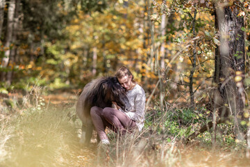 A young woman and her shetland pony cuddle together in a forest in autumn outdoors