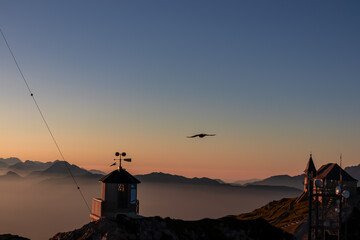 Birds flying around weather station with panoramic sunrise view from Dobratsch on Julian Alps and...