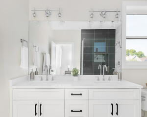 A bathroom with a white vanity cabinet, white marble countertop, and silver faucets with a view of the tiled shower through the mirror.