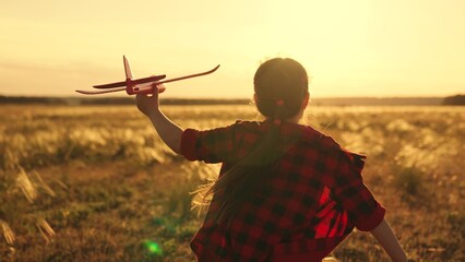 Happy kid runs with toy airplane on field in sunset light. Child play toy airplane. Little girl...
