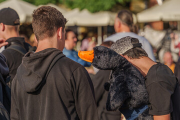 A man in a crowd wears a plush duck head. The scene is lively, capturing the essence of public gatherings. This photo captures the concept of uniqueness and standing out