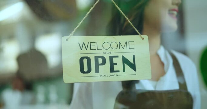 Attractive woman turning sign on fronton glass door store. Close-up on sing hanging at cafe door store. Small business concept.