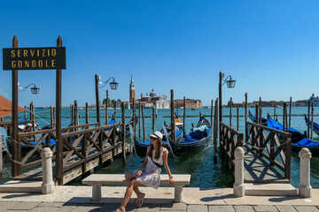Tourist woman and sign indicating Gondola service at Saint Mark square in Venice, Veneto, Northern Italy, Europe. Scenic view of San Giorgio di Maggiore church. Romantic vacation in Venetian Lagoon - obrazy, fototapety, plakaty