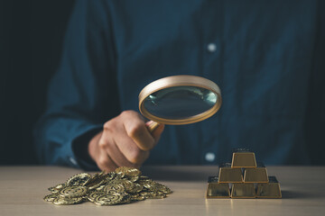 Businessman using magnifier and decide between gold and money coin for stock market fund currency...