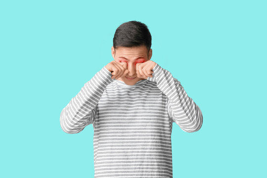 Young man rubbing eyes on light blue background
