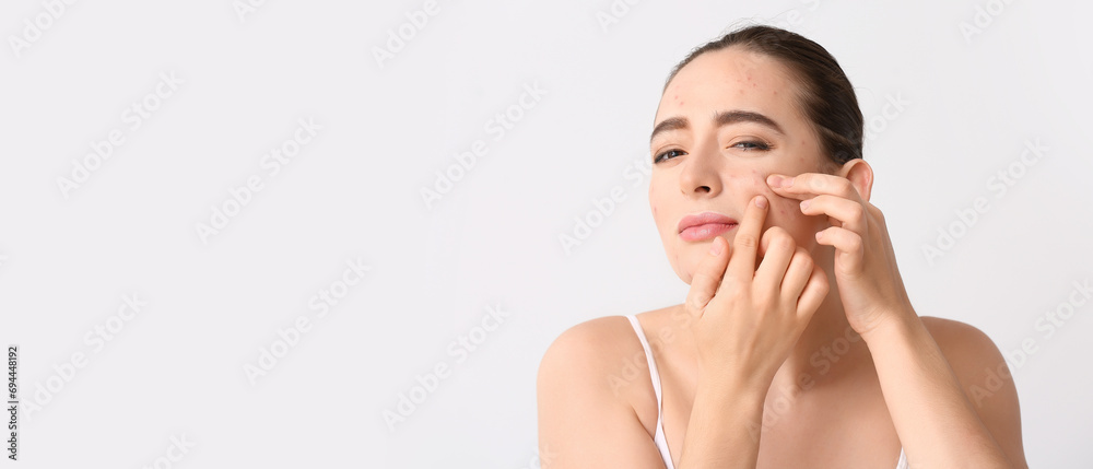 Wall mural Young woman with acne problem squishing pimples on light background with space for text