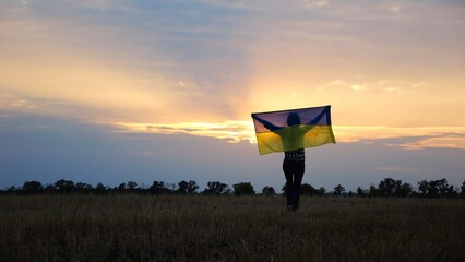 Ukrainian woman going with raised flag of Ukraine above head on wheat field against background of...