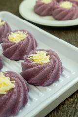 bolu kukus ubi ungu or purple sweet potato steamed sponge cake with grated cheese on top, served on a white plate.