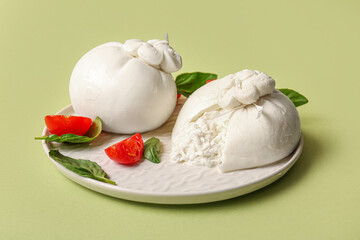 Plate with tasty Burrata cheese on green background