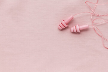 Reusable silicone earplugs pink color on colored cloth background, copy space. Soft, flexible ear plug on cord, for swim, sleep, against noise, protect hear, monochrome top view, minimal trend