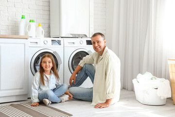 Mature man with his little granddaughter sitting in laundry room