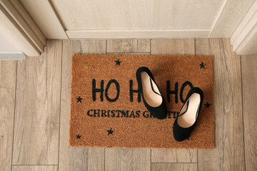 Doormat with Christmas greeting and shoes in hall, top view