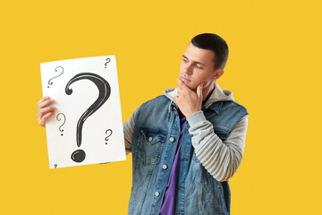 Wondering young man holding paper with question marks on yellow background