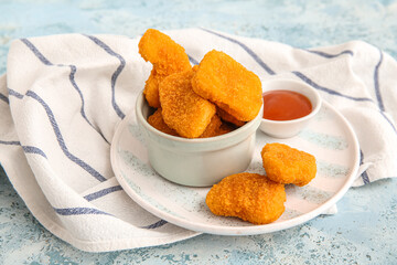 Bowl with tasty nuggets and sauce on blue background