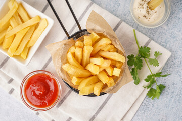 Deep fryer basket with tasty french fries and sauces on white background