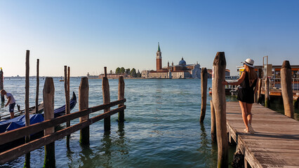 Tourist woman on wooden fotsteg with scenic view of San Giorgio di Maggiore island in Venice, Veneto, Northern Italy, Europe. Gondolas moored by Saint Mark square, Venetian Lagoon. Tranquil atmosphere © Chris