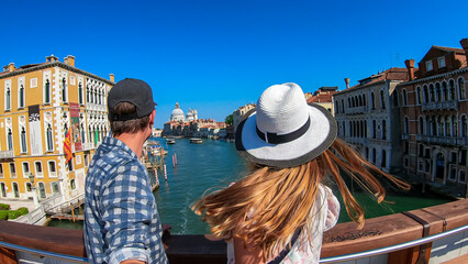 Tourist couple standing on top of famous Rialto bridge overlooking the Canal Grande in Venice,...