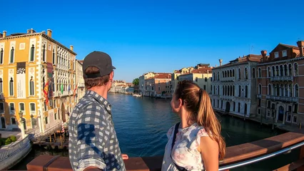 Papier Peint photo Pont du Rialto Tourist couple standing on top of famous Rialto bridge overlooking the Canal Grande in Venice, Veneto, Northern Italy, Europe. Female model is wearing black dress. Romantic luxury summer vacation
